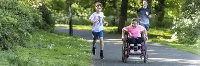 three children on a park pathway one of them in a wheelchair